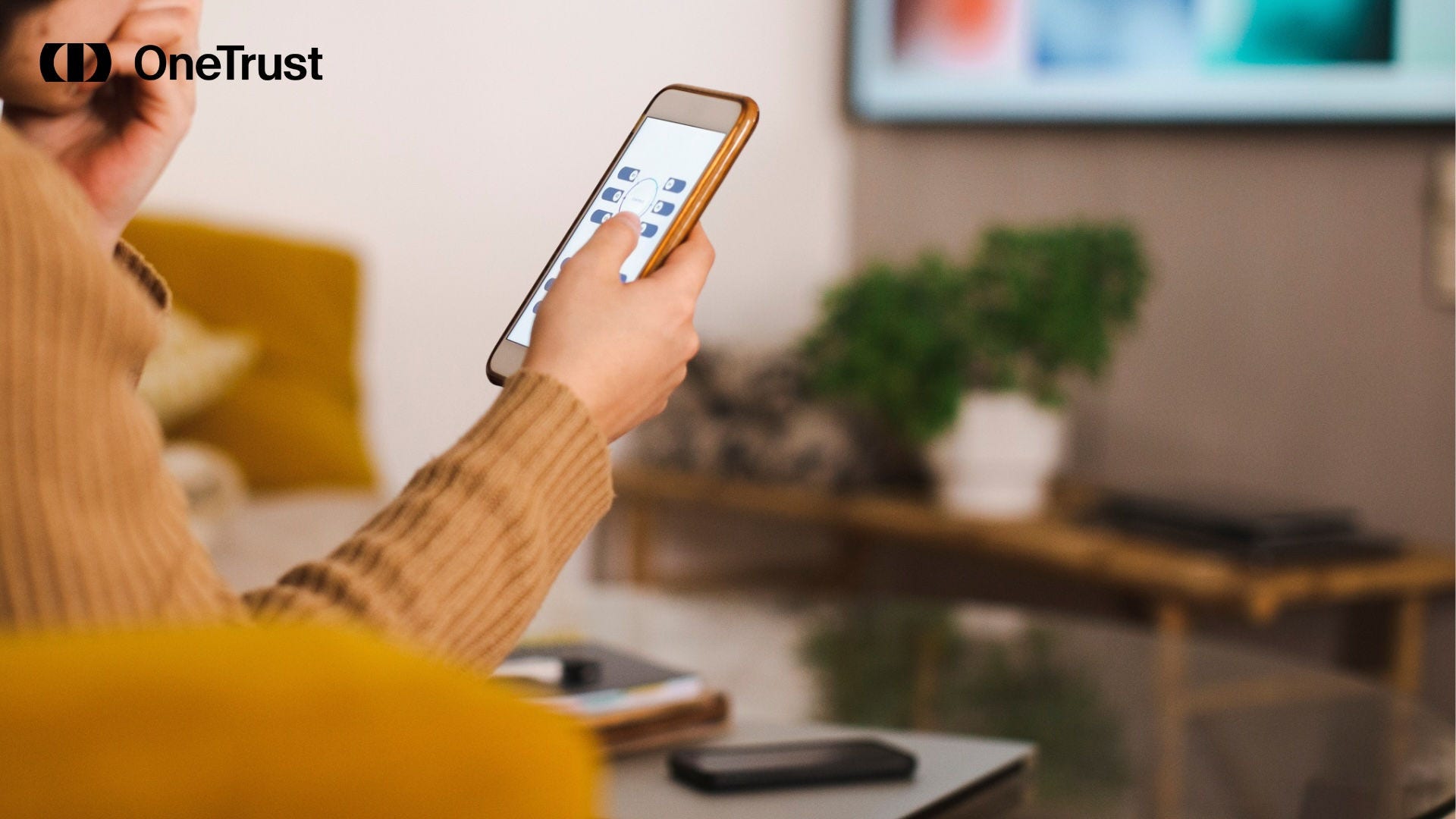 Person using a smartphone to control a television in a living room, with the OneTrust logo in the upper-left corner.