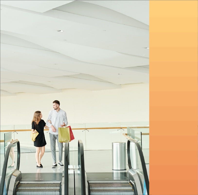 A shopping couple prepare to step onto a mall's escalator.