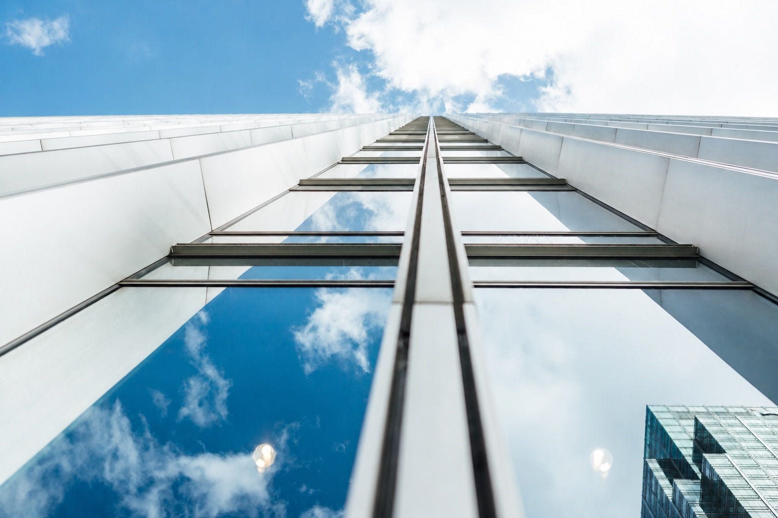 Looking up at a modern glass-and-white commercial building against a blue sky with clouds. 