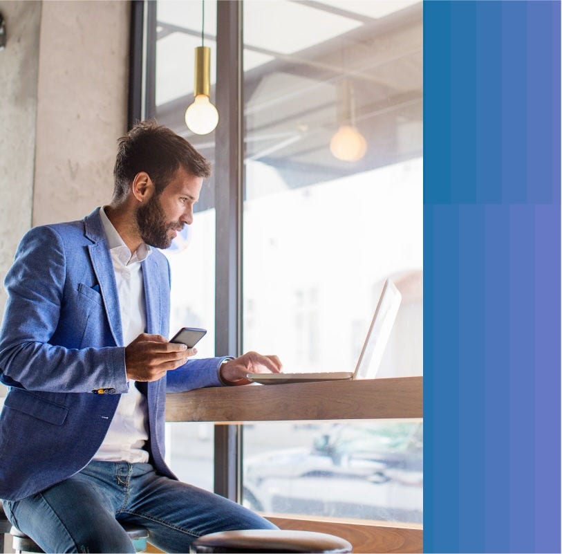 Businessman working on his laptop while holding his cellphone.