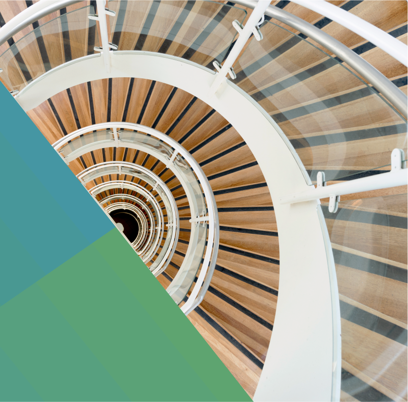 photo of a spiral staircase with glass railing and white metal barristers. The viewer is looking down from the top of the staircase so that the steps form a semi circle.