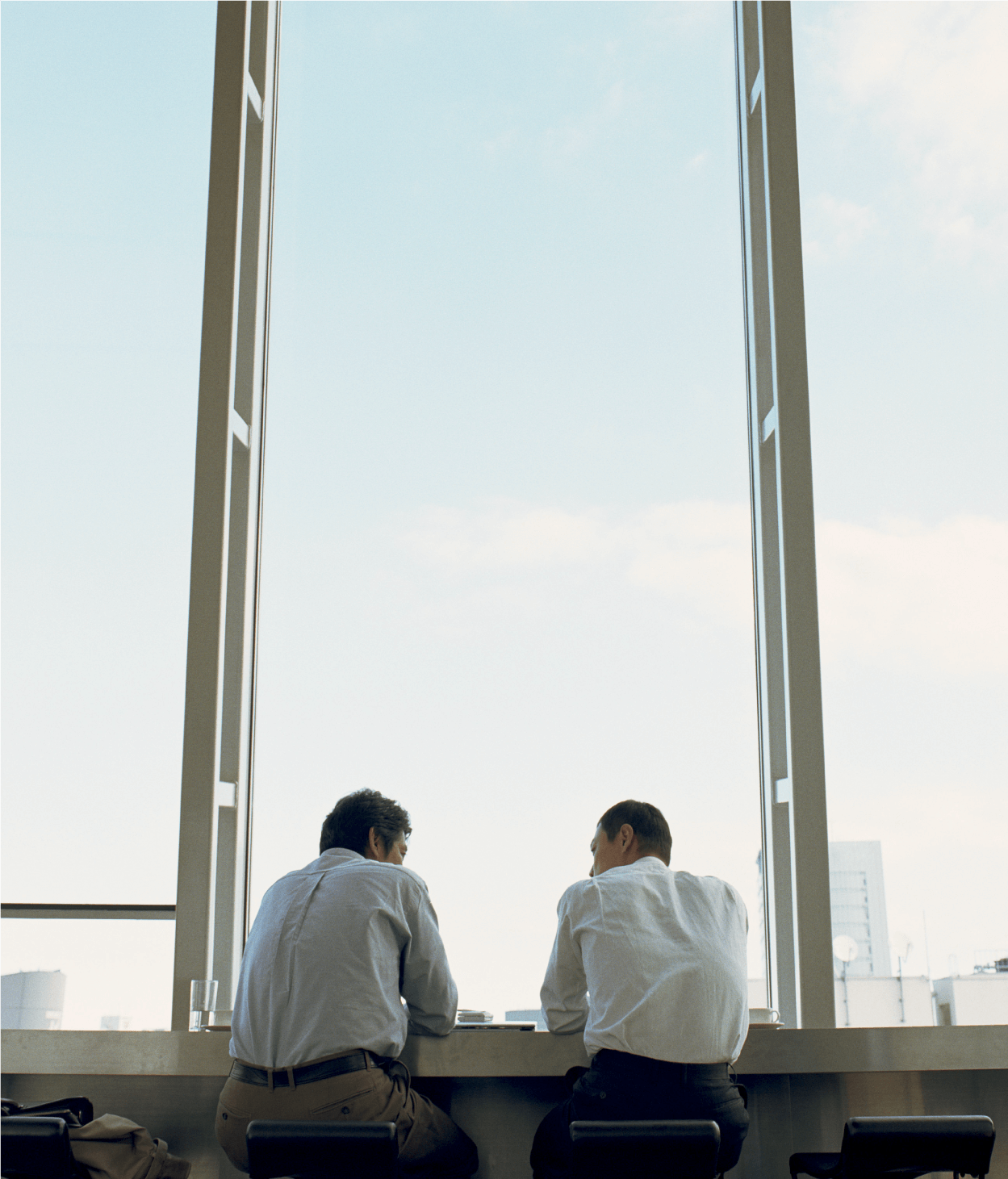 Two male coworkers speaking by a window