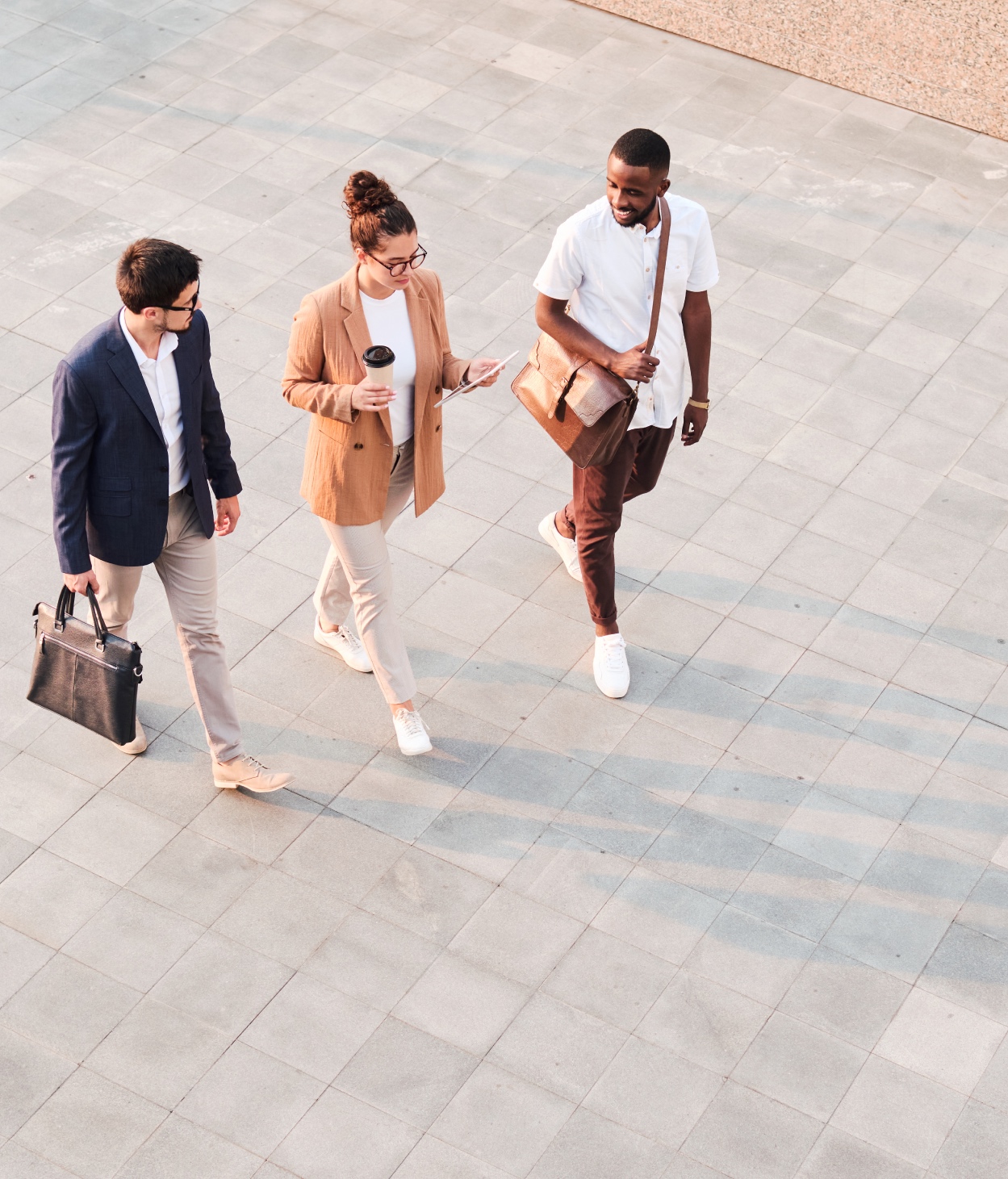 A young woman and two young men chat as they walk across a stone court.