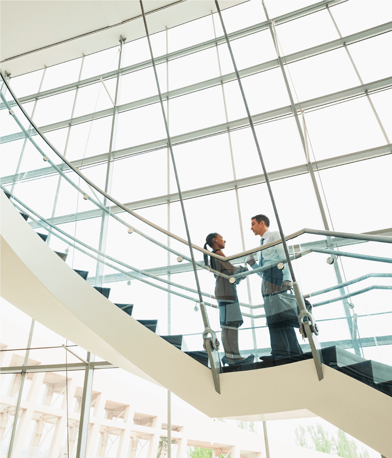 photo of two office employees having a conversation on a flight of stairs in a lobby in front of a large glass windows.