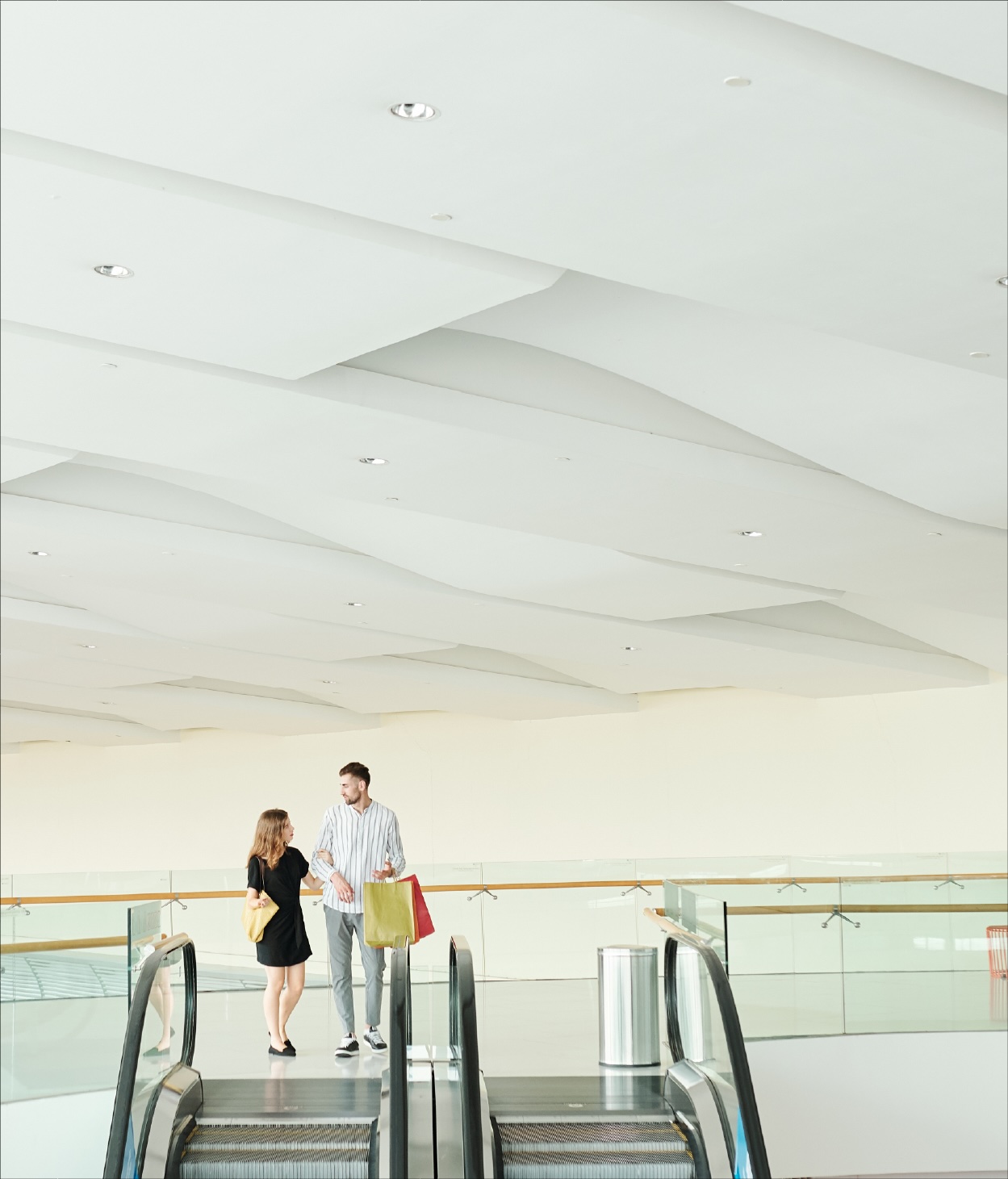 A shopping couple prepare to step onto a mall's escalator.