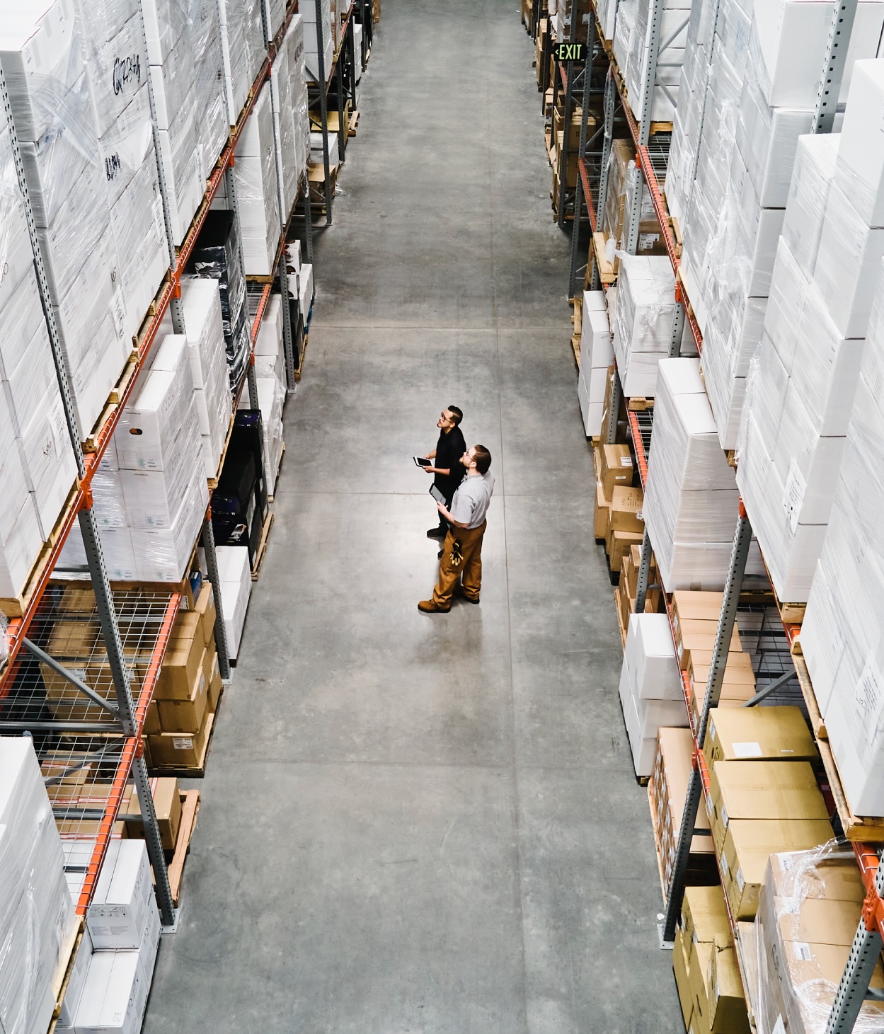 Warehouse employees examine boxed products in a wide aisle.