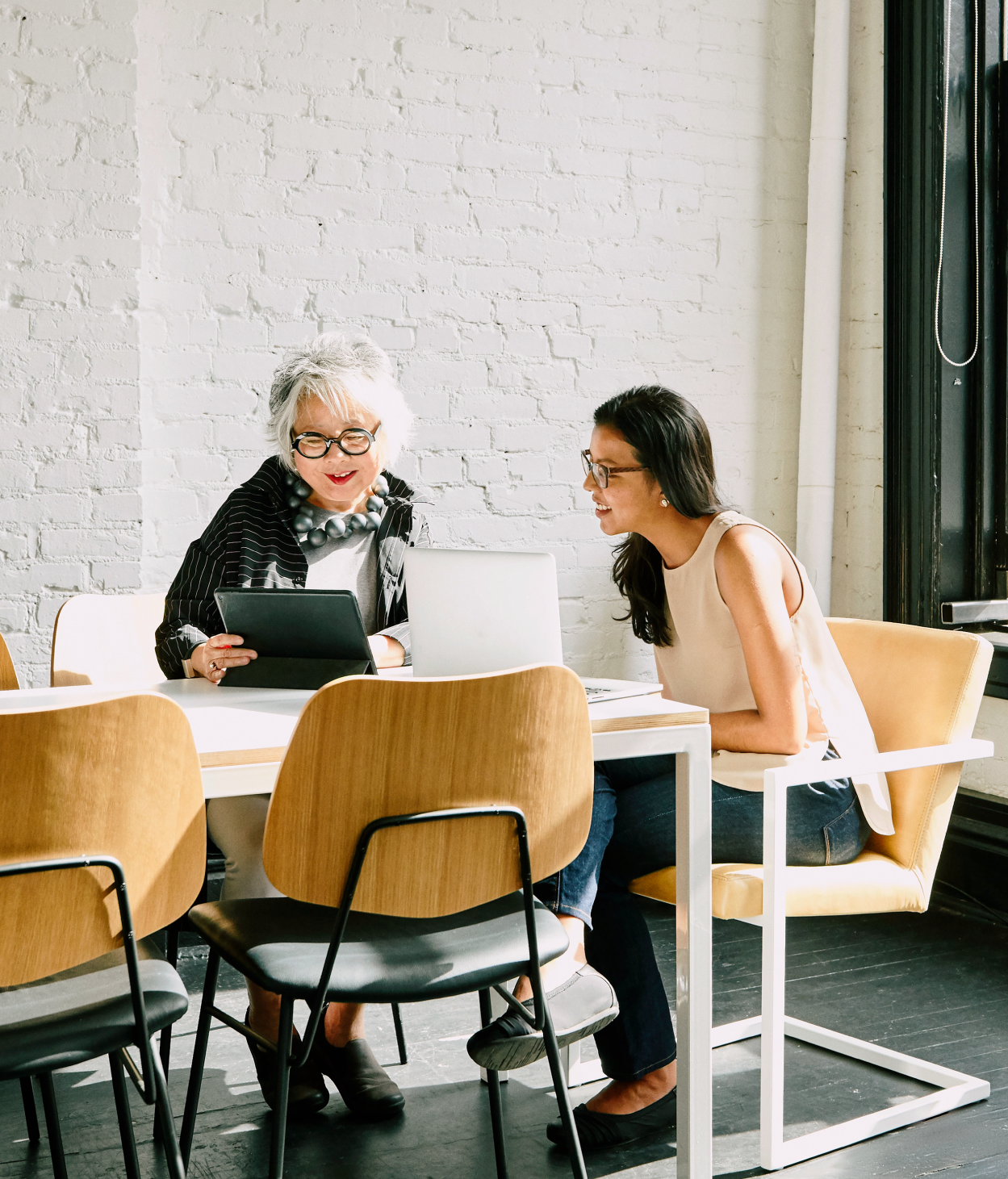 Two businesswomen collaborate on a project in an office conference room.