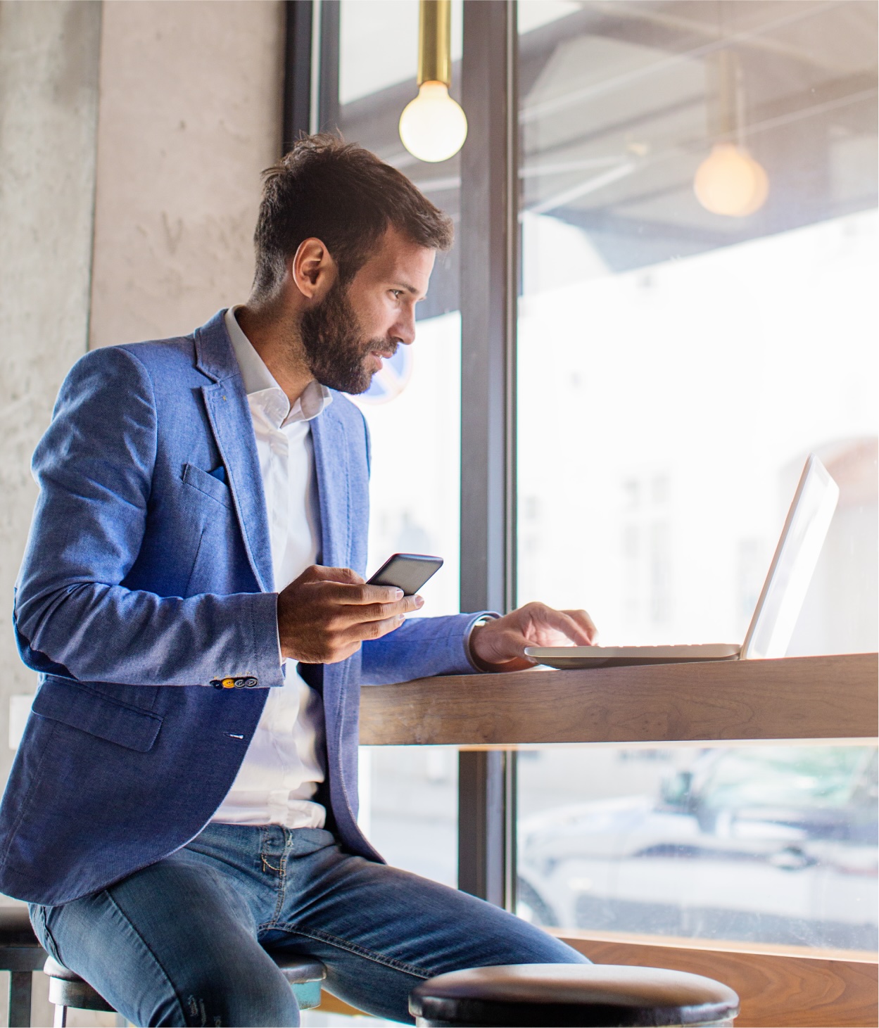 Businessman working on his laptop while holding his cellphone.