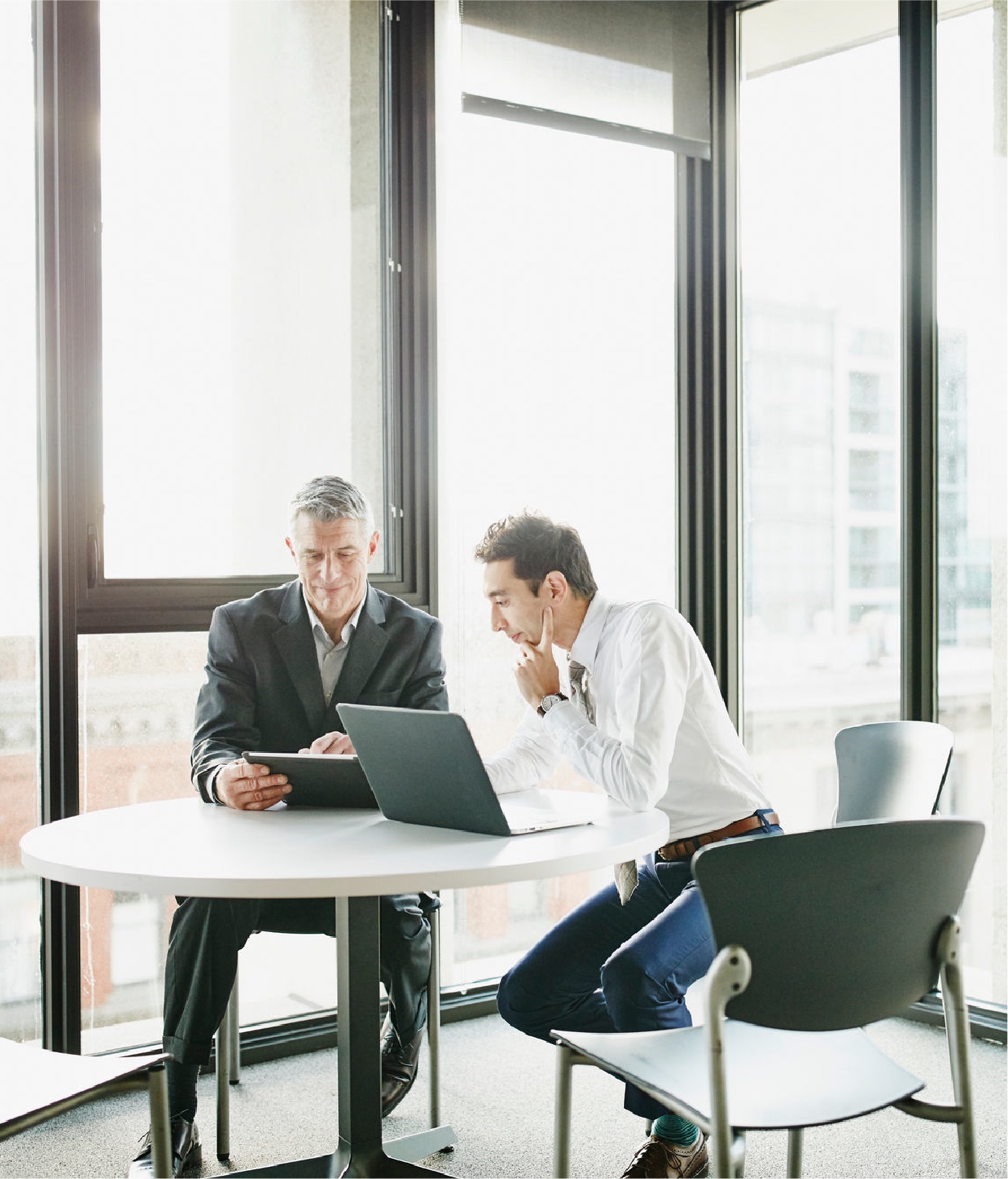 Two men in business attire hold a remote meeting from an office break room.