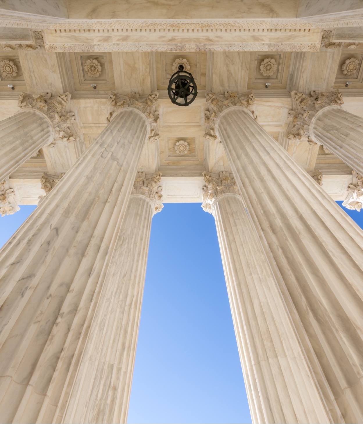 Point-of-view photo of someone looking up at the roof of a Neoclassical courthouse's entrance.