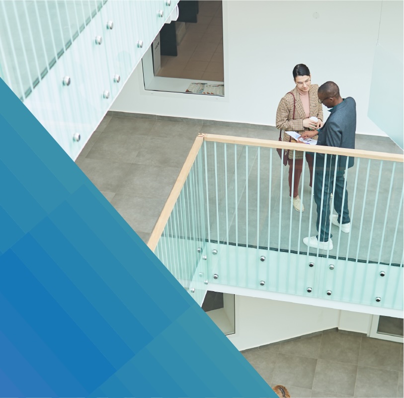 Two businesspeople examine notes on an office walkway