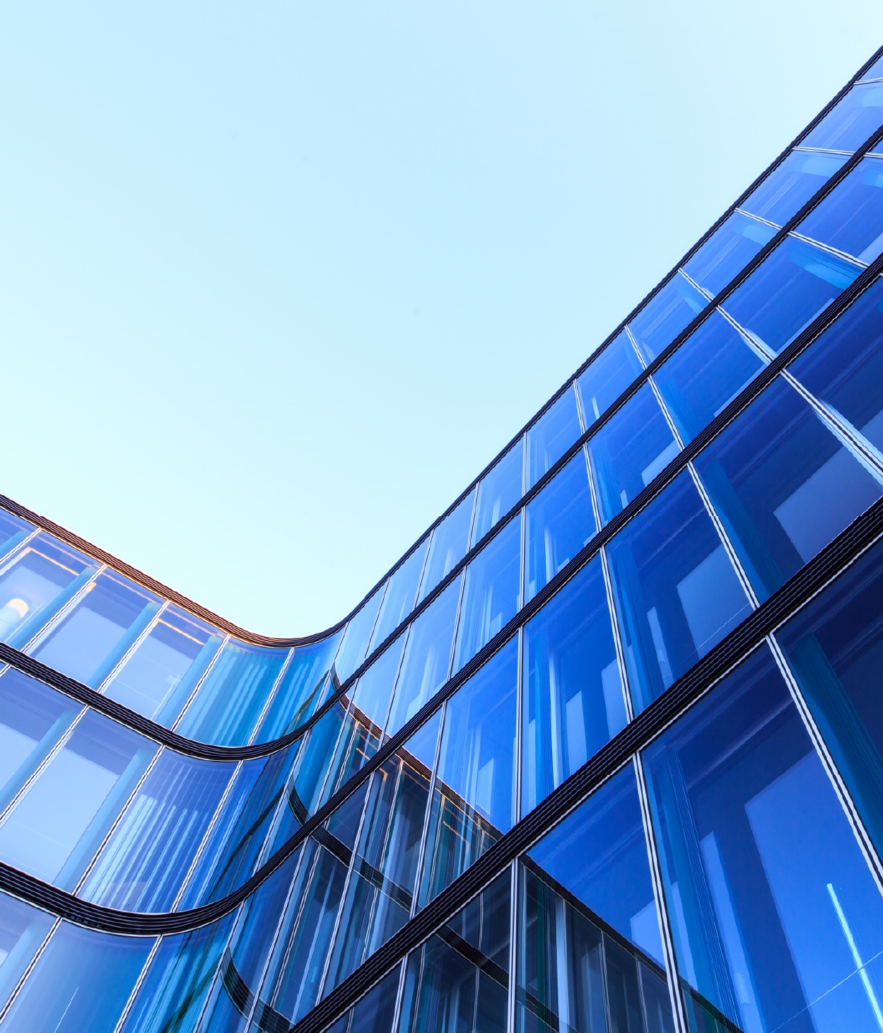 Low-angle photo of the curved glass façade of an office building.
