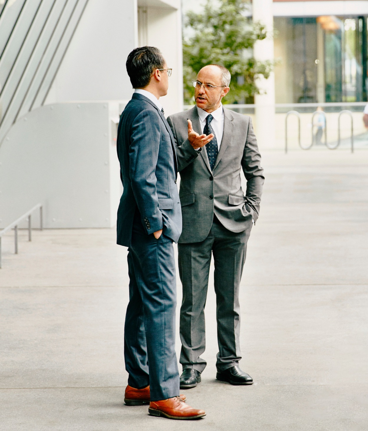 Two businessmen hold a conversation outside of an office building.