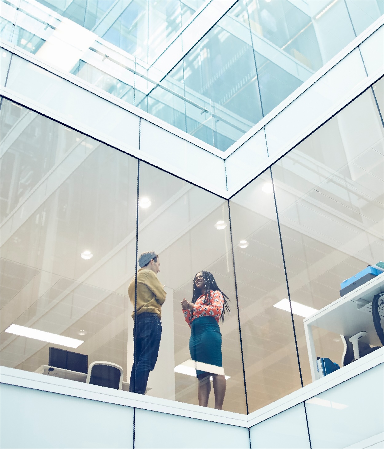 Low-angle photo of two colleagues talking in their office through a glass wall. 