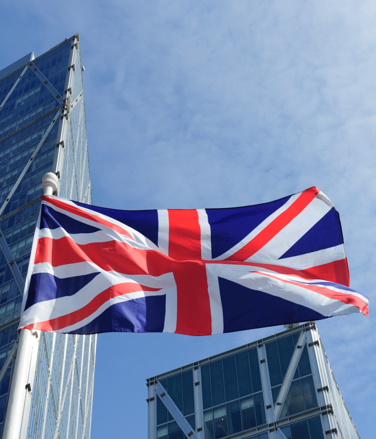 The U.K. flag flying in front of a pair of skyscrapers.