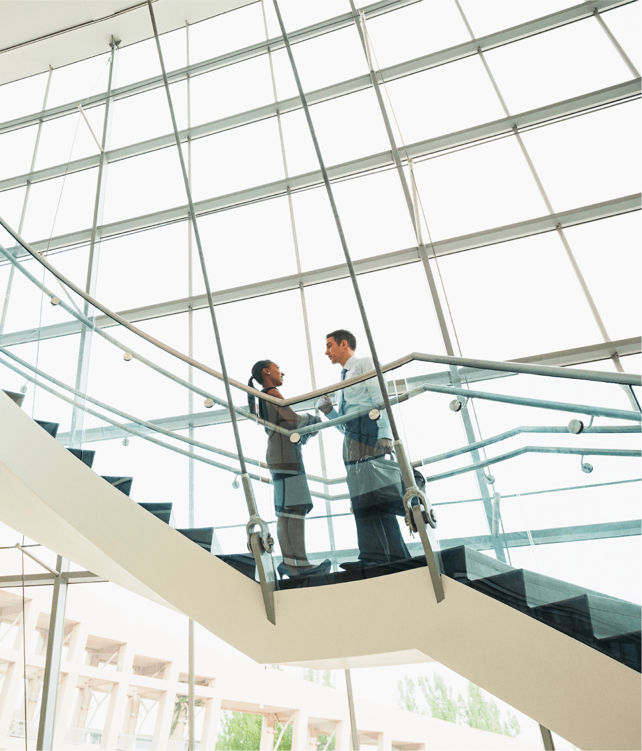 photo of two office employees having a conversation on a flight of stairs in a lobby in front of a large glass windows.