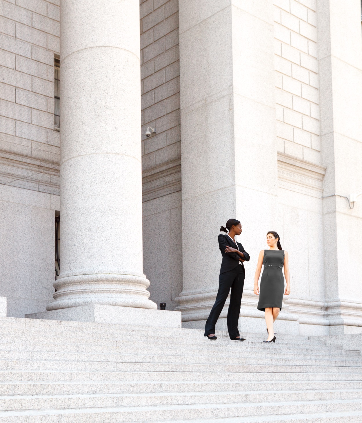 Two female lawyers converse on a courthouse's front steps.