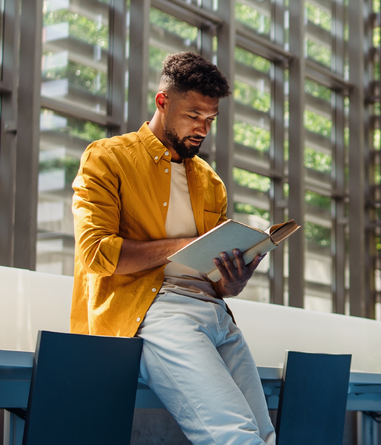 Young Black professional reading a book in a naturally lit office lobby.