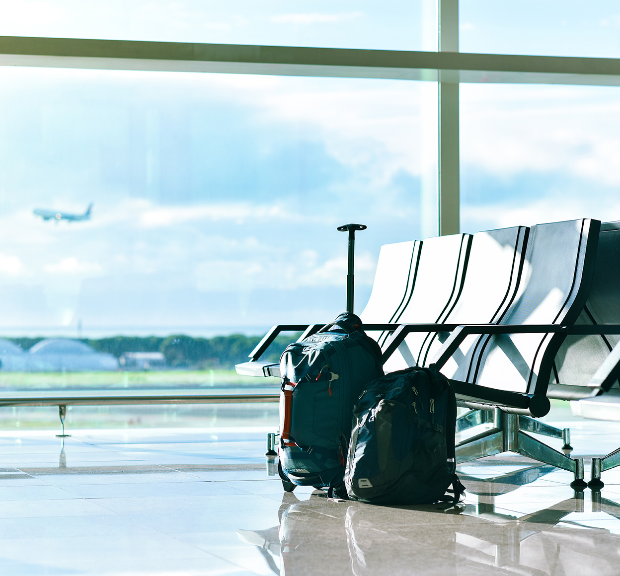 Luggage at gate of airport with plane flying outside in the background