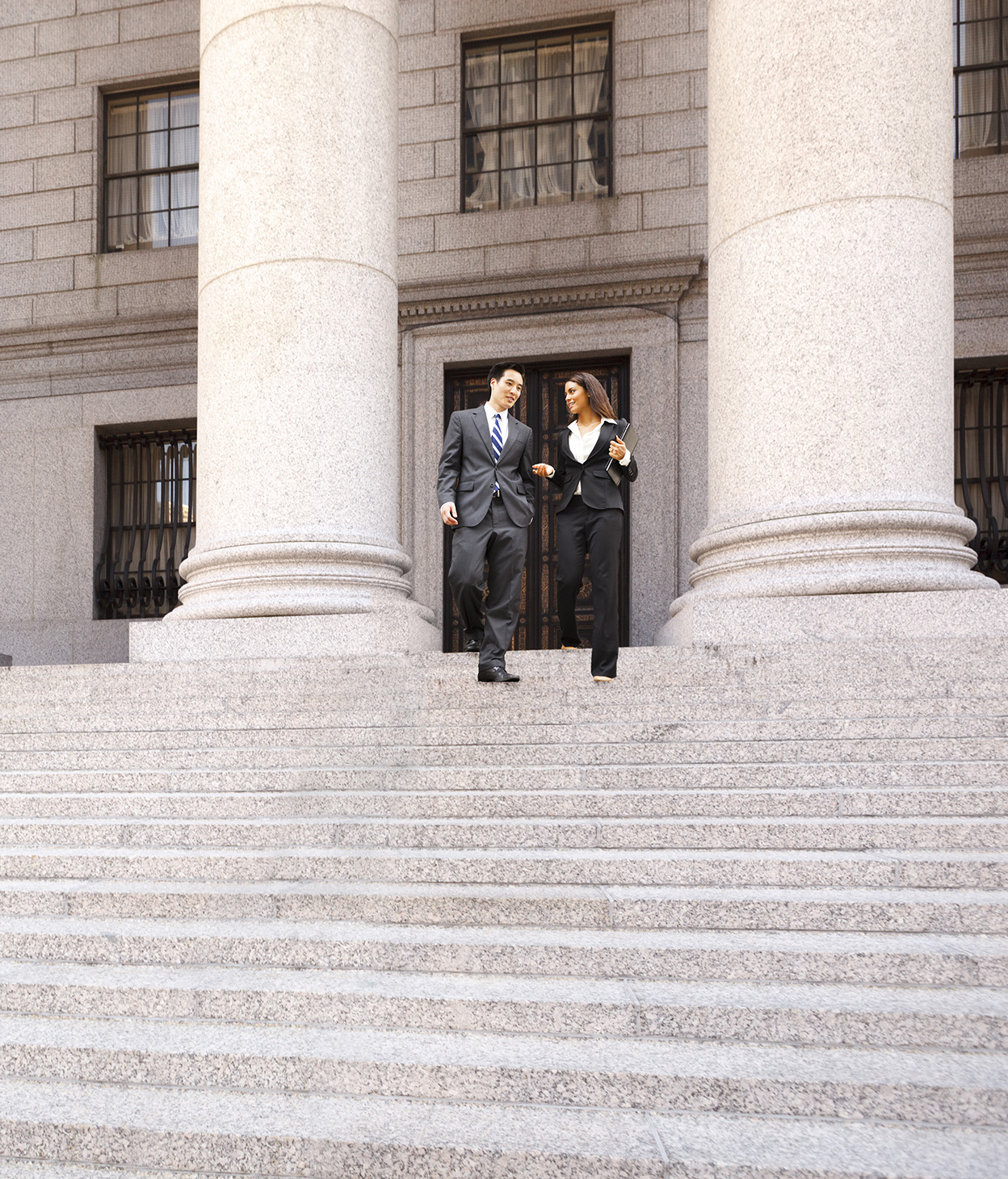 Une avocate et son client descendant les escaliers en pierre d’un palais de justice.