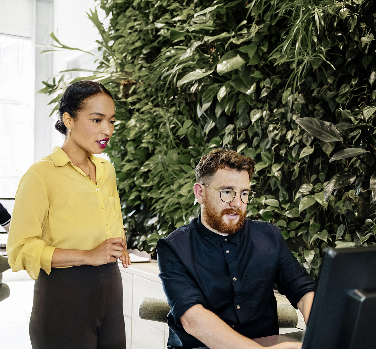 two people looking at a computer with a living plant wall in the background