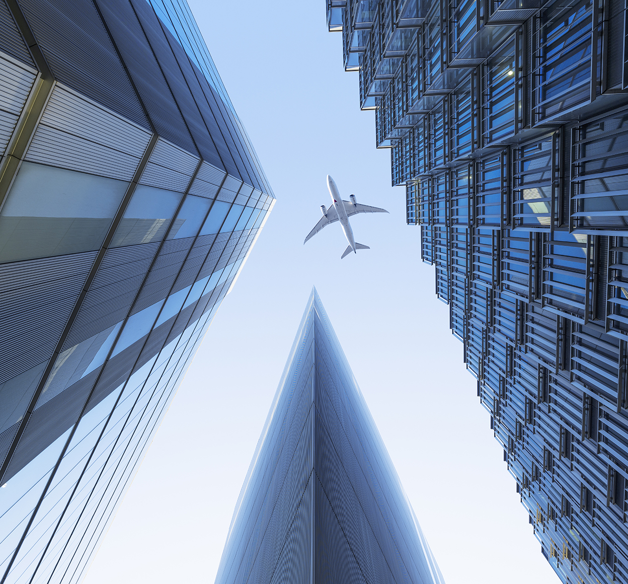 Ground photo looking up at an airliner flying over a group of city skyscrapers