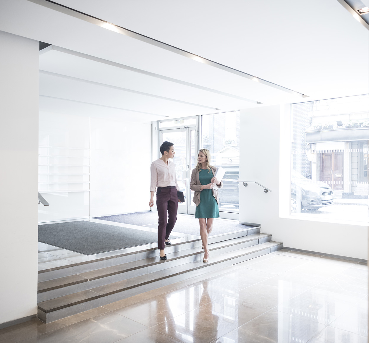 Businesswomen converse as they walk into an office lobby