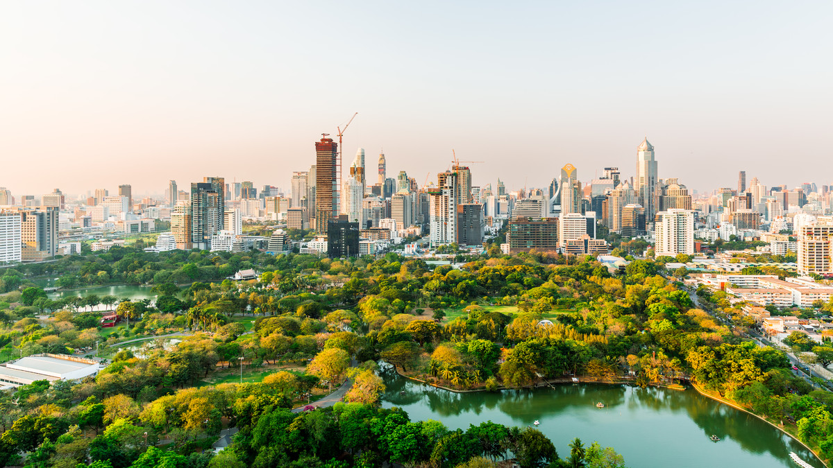 Aerial view of Bangkok’s skyline beyond a lush city park and lake.