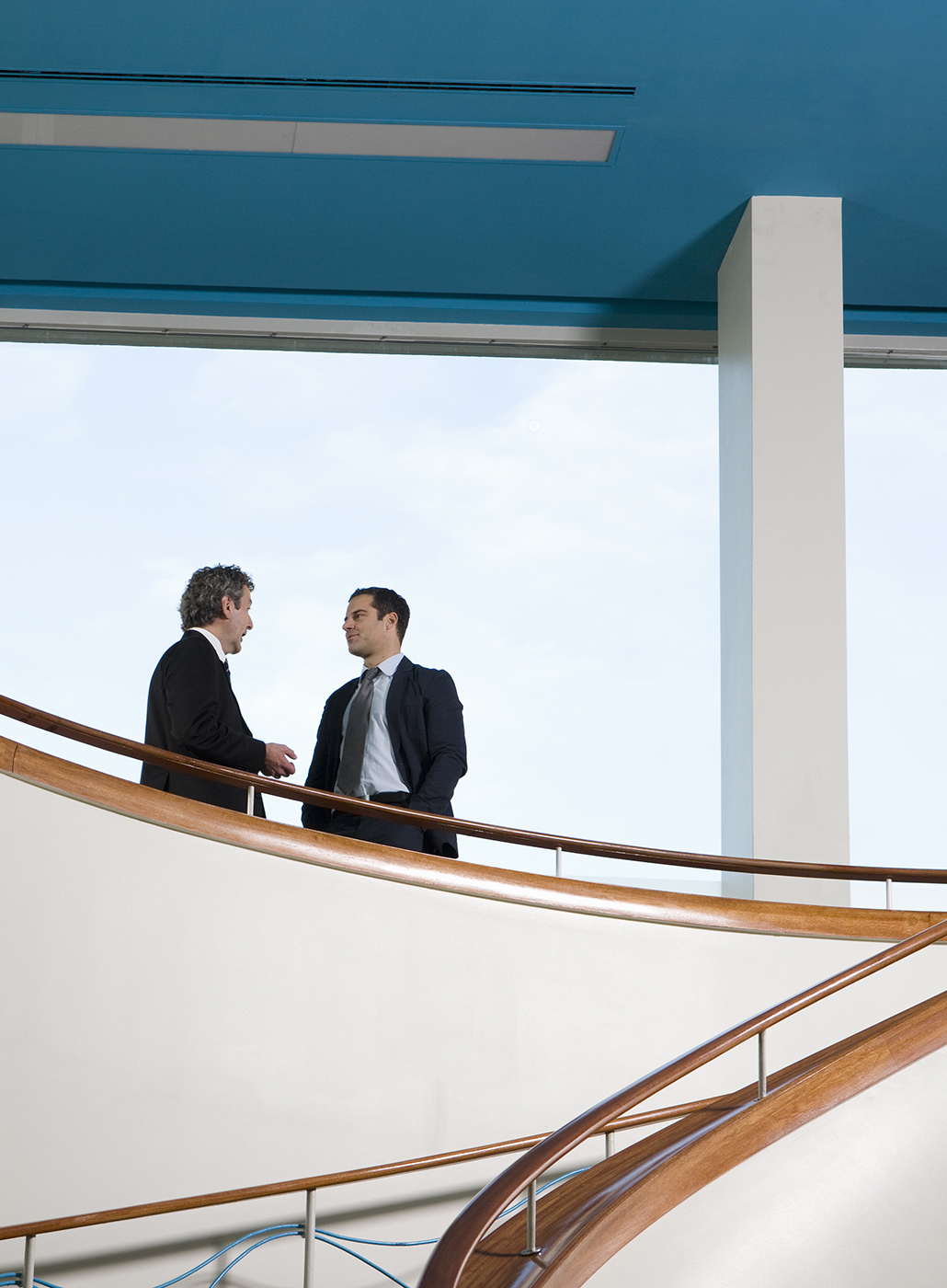 Two businessmen converse on a balcony.