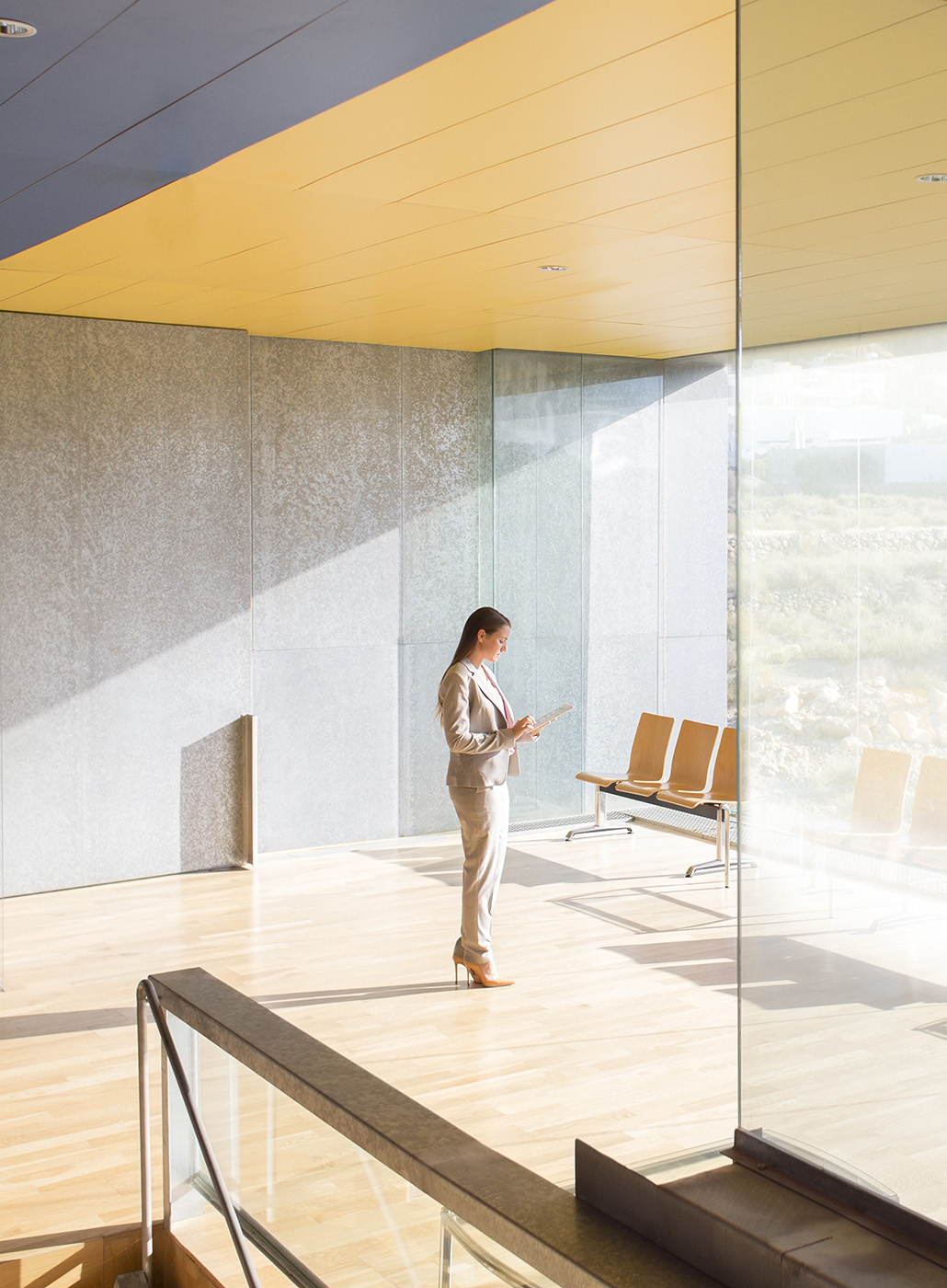 Businesswoman works on her digital tablet in a sunlit office lobby.