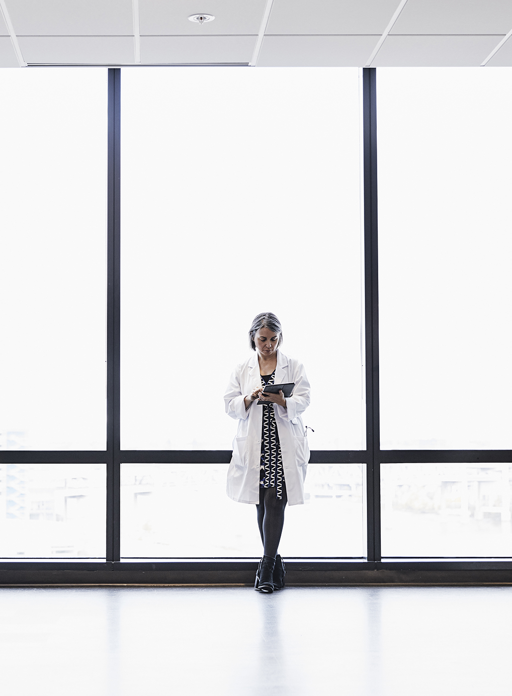 Female doctor using a digital tablet in front of large windows.