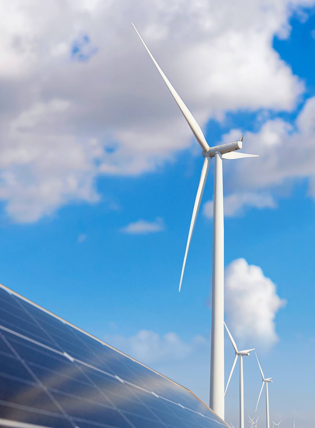 Low angle photo of solar panels and a wind turbine at a renewable energy station.