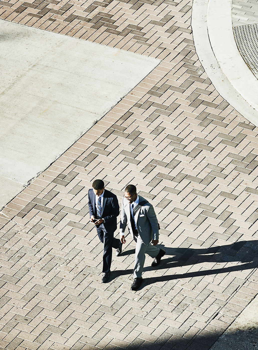 Overhead view of two businessmen in discussion walking across downtown street.