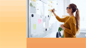 Woman writing on post-it notes stuck to a whiteboard with OneTrust orange colors to the left and bottom.