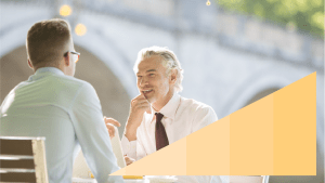 Two men in business attire chatting outside of a cafe with the OneTrust yellow gradient triangle to the right corner of the image
