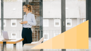 OneTrust thumbnail of a woman wearing business attire holding a remote while in a meeting room with a yellow step gradient triangle in the bottom right corner.