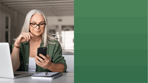 A woman with glasses sitting at a desk while grinning at her phone and a OneTrust green to the right of the image.